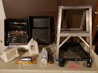 Photo of assorted home renovation tools including paint trays, ventilation grilles, roller cover, scraper, and a small step ladder.