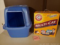 Blue covered cat litter box with hood and front entry door beside large yellow box of Arm & Hammer Multi-Cat cat litter.