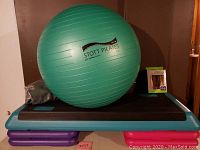 Photo of teal and purple exercise step platform with 'STEP' on top and the green Stott Pilates exercise ball resting on it alongside a grey skipping rope pouch.