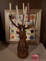 Frontal view of deer candle holder with four different colored candles and framed picture behind