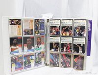 Photo shows binder with vintage basketball cards, each in plastic sheet protectors, visible players include Hawks and Jazz team members.