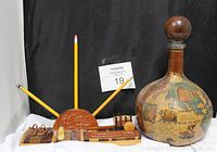 Photo showing both the leather-wrapped decanter bottle with old-world map design and the Costa Rica handcrafted pencil display souvenir on a white cloth against a black backdrop.