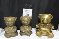 Photo showing two brass teddy bear bookends and one larger brass teddy bear sculpture all sitting together against a black background.