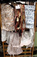 Seven vintage aprons hanging on a rack in various floral and striped patterns, hip-length, mostly cotton