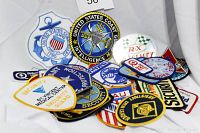 Photo showing a pile of assorted patches featuring United States Coast Guard, Coast Guard Intelligence, and Security Guard patches among others, plus a small decal.
