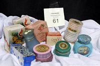 Shows six items including boxed sachets and assorted perfume bottles in different colors and designs, arranged on white fabric.
