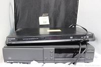 Two electronics stacked: top is Panasonic DVD and CD player, bottom is Philips CD player. Both black, with cords attached.