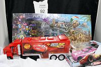 Shows Lightning McQueen 18-wheeler truck in front of two-sided Cars puzzle in original packaging and pink Flipdover Pull & Race Car boxed toy.