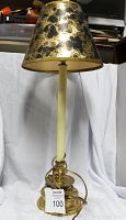 Vintage brass based table lamp shown from the front with a distinctive black and gold mottled lampshade and cream colored stem.