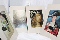 Three art books displayed upright showing cover or inside glossy page reproductions of classical portraits including a Renaissance man and a woman with a large hat.