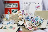 Box of assorted postage stamps, loose and on paper, with two paperback books and multiple pamphlets behind them.