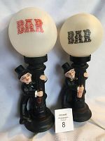 Front view of two vintage bar lamps with round white globes labeled 'BAR' in red and black, each featuring a man figurine clinging to a pole base.