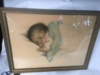 Framed vintage print showing full view of the artwork depicting a sleeping baby wrapped in a blanket, set in a neutral frame.
