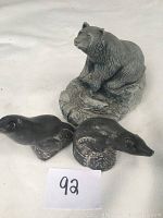 Grey sandstone bear with fish carving and two smaller black sandstone seal carvings on white background with lot number card
