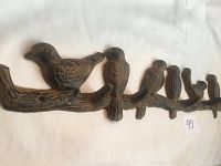 Close-up of metal coat rack showing bird figures and hooks, highlighting condition and design.