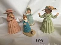 Group photo of 4 small collectible vintage figurines showing dresses and hats