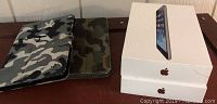 Two camouflage magnetic protective cases with two white Apple iPad Mini boxes on a table