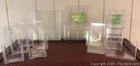 Several clear plastic brochure holders in various sizes and configurations placed on a wooden shelf. Some holders have multiple compartments; others are single-compartment.