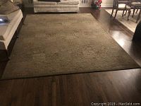 Full view of large beige and brown patterned area rug on hardwood floor, showing its scale relative to surrounding furniture.