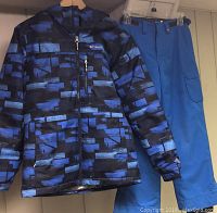 Photo of youth Columbia ski snowboard jacket and blue Under Armour snow pants hanging on hangers.
