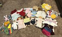 Full overview of three dolls with multiple pieces of doll clothing, some stained, arranged on carpet