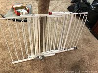 Two white metal safety gates laid on carpet, one larger and one smaller, showing adjustable components and locking mechanisms.