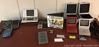 Photo shows various electronics including calculators, a gray Game Boy Advance SP, two iPods, some mobile phones, Nintendo DS consoles, and game cartridges spread out on a table.