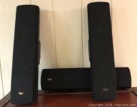 Front view of two tall Klipsch tower speakers with black fabric grille covers and Klipsch logo on each, alongside a center channel speaker showing dual gold woofers and tweeter.