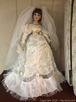 Porcelain wedding doll in full detailed white gown with veil shown.