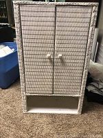White wicker cabinet with two magnetic doors and a bottom shelf, shown from front view on carpeted floor with surrounding items.