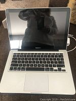 Open Apple MacBook Pro laptop showing screen and keyboard from front view, screen off, reflective