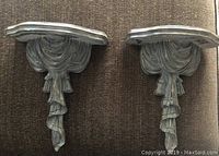 Photo of both matching decorative wall sconces showing detailed tassel and draped fabric carved design with flat surface for holding candles or decoration.