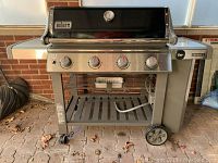 Front view of grill assembled showing four control knobs, side shelves, cart, wheels, gas hose