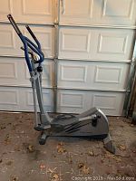 Side profile view of the full silver and blue elliptical trainer in a garage setting