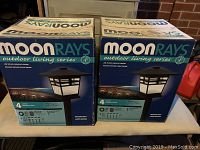 Two unopened boxes of Moonrays Outdoor Living Series landscape lights showing packaging and key features.
