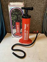 Photo of orange and black Intex Double Quick III manual air pump with flexible hose and two nozzles, shown next to its original box.