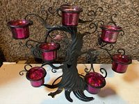 Black metal tree candle holder with 7 red reflective tea-light candle holders arranged on branches and base, face on trunk visible.