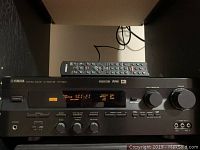 Front view of Yamaha HTR-5240 AV receiver with remote control placed on top, showing the power button, display panel, and control knobs.