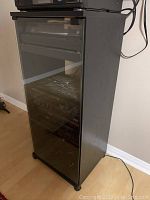 Front and side view of the black stereo cabinet with glass door closed, showing the full height and design.