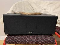 Front view of the Polk Audio CS245i center channel speaker with black fabric grille and coiled speaker wire on top.