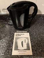 Photo of the black Toastess cordless electric jug kettle with its instruction booklet placed on a kitchen countertop.