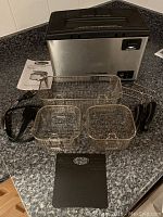 Bravetti deep fryer with three fry baskets, three basket handles, divider panel, and instruction manual laid out on countertop