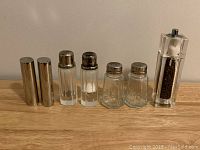 Front view of all seven units showing different materials and shapes of salt and pepper shakers and the pepper grinder
