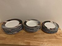 Photo showing the 3 stacks of plates including the 8 dinner plates, 8 bowls, and 7 small plates, all featuring a white center with multi-colored striped rims.