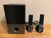 Front view of subwoofer and two satellite speakers with cables.