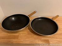 Front view of non-stick wok and frying pan showing black interior and wooden handles.