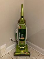 Front view of green Eureka upright vacuum cleaner plugged into wall outlet on tiled floor.