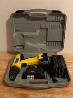 Power Fist 18V cordless drill, spare battery, charger, and some drill/screw bits inside a plastic gray carrying case.