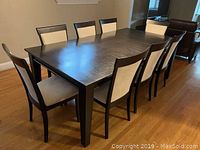 Front angle view of dark brown dining table with eight chairs arranged around it
