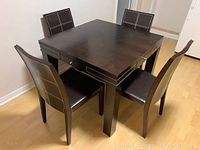 Assembled dark wood table with four matching leather chairs around it, top in place